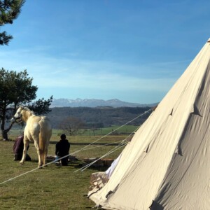 Bivouac chevaux, le tipi en formule "glamping" avec vue sur le massif du Sancy et 2 personnes en train de préparer le barbecue